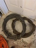Photo showing two coiled grey pneumatic air hoses on a floor next to a door.