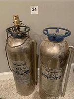 Two vintage General fire extinguishers repurposed as lamp bases with blue handwheel tops and metal bodies.