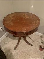 Top view of round wooden table showing multiple stains, scratches, and water rings on the surface with one drawer closed and wooden central pedestal base.