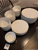 Photo showing stacks of white plates and bowls on a table, with various sizes visible.