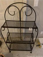 Front view of 3 shelf wrought iron unit showing mesh shelves and scroll design at the top and sides.