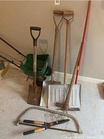 Photo showing the full assortment of yard tools including shovel, shovels, mattock, rake, hedge shears and spreader placed against wall