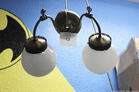 Front view showing the two white glass globes, curved antique brass arms, and mounting plate against a blue background.