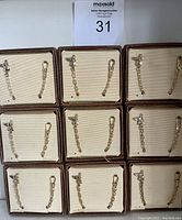 Nine individually boxed dog watch fobs arranged in three rows of three. Each fob has a short chain and clip, displayed on cream-colored cushioned box interior with brown border.