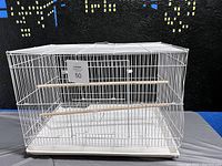 Front view of white metal bird cage showing overall cage structure, two wooden perches, and multiple front access doors