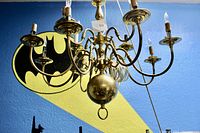 Frontal view of brass candelabra chandelier against a wall with Batman shadow art