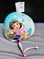 Front side of children's helmet featuring Dora the Explorer and three cartoon pets with hearts and flowers background.