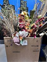 Photo showing a box filled with assorted dried flowers including pale orchid-like petals, broad leaves, and various grasses.