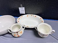 Photo showing two plates, two handled cups, one large bowl with floral leaf and gold rim patterns