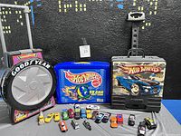 Three Hot Wheels carrying cases, including Goodyear tire case, blue 48-car Hot Wheels case, and black hard Hot Wheels case with model sports car.