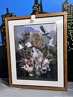 Framed large print showing various wildlife animals including bear, moose, wolves, and birds, against a mountainous background with wooden frame