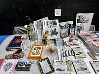 Full view of the mixed vintage estate items arranged on a table showing figurines, glassware, photos, books, and assorted collectibles