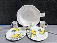 Front view of full set: large white bowl with beaded edge and lemon decorated plates, mugs, and bowl.