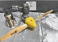 Photo showing the RC engine with attached wooden propeller and yellow spinner, and the metal threading bit placed beside them.