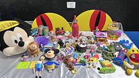 Wide image of all toys showing layout and variety including plush Mickey Mouse head, lion, toy train, snowglobes, small figurines, clapper and handheld toys, water bottle, and novelty toys in lots of colors.
