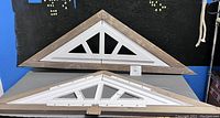 Two triangular decorative pieces stacked one above the other; wooden frames with white plastic geometric inserts