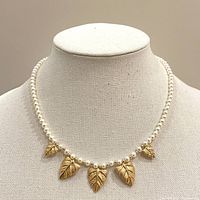 Full front view of the pearl necklace with five gold leaf charms displayed on a fabric bust