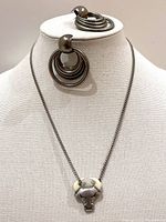 Full view of necklace and earrings displayed on a white stand. Necklace shows bull pendant with horns and multi hoop earrings behind it.