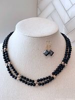 Front view of dual strand black beaded necklace with champagne crystal accents paired with sterling silver earrings with black crystals, displayed on jewelry stand.