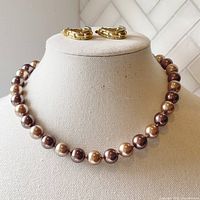 Full view of knotted faux pearl necklace in chocolate brown shades and clip-on hoop earrings on display bust.