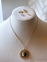 Green amber-like faux pendant necklace on manneken bust with matching screw-on earrings displayed.