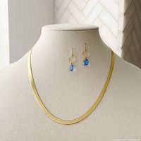 Front view of gold over sterling silver necklace and art deco blue cubic zirconia earrings on display stand