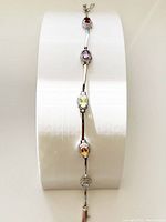 Full length of the linked bracelet showcasing five oval-cut gemstones in different colors with polished silver tone metal links and fold-over clasp.
