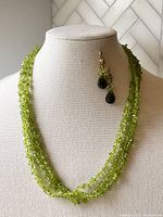 Front view of multi-strand peridot necklace displayed on bust with matching earrings.