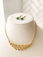Photo showing gold tone necklace with pea-shaped pattern and matching faux emerald drop earrings on display bust.
