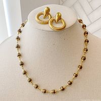 Full view of vintage grey faux pearl necklace with gold coil accents alongside vintage Avon clip-on door knocker earrings on display bust