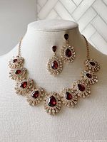 Front view of Monet necklace and matching earrings displayed on bust form, showing pear-shaped red faux ruby pendants surrounded by clear rhinestones on gold tone setting.