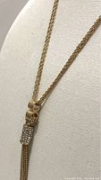 Close-up side view of the gold dual strand lariat necklace showing the rhinestone clasp and tassel detail