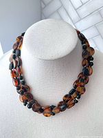 Triple strand faux amber and black bead necklace displayed on a white bust showing multi-strand layering and bead shapes.