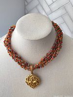 Full view of the multi-strand faux carnelian necklace with gold deer pendant displayed on a white bust stand.