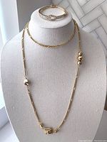 Full view of the vintage bracelet displayed on a stand alongside the long gold tone decorative chain necklace featuring various bead shapes.