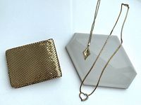 Photo showing the vintage gold textured wallet alongside two gold tone necklaces with pendants, displayed on a white surface.
