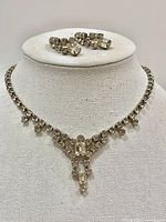 Front view of vintage rhinestone necklace and matching earrings displayed on white stand.