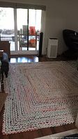 Photo showing full view of multi colored woven area rug laid out on hardwood floor in living space with sliding glass door and furniture.