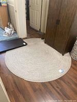 Full view of round woven area rug placed on wooden floor near doorway and cabinet.