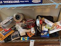 View of various mounting and packing supplies including tape rolls, Velcro strips, and adhesive picture hangers on shelf