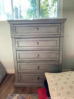 Front view of wood dresser with five drawers, showing drawer fronts and knobs.