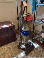 Full upright Dyson vacuum cleaner on carpet, showing the unit with handle, wheels and base.