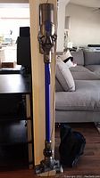 Front view of Dyson cordless vacuum cleaner mounted on wall with blue wand, motor, and head.