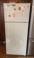 Front view of the white GE top freezer refrigerator showing magnets and stickers on freezer door.