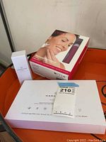 Photo of Hanacure All-In-One Facial Kit box prominently showing packaging details and PMD Personal Microderm Pro facial device box with image of woman using device