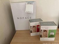 White NuFACE box with two sealed attachment boxes (Wrinkle Reducer red and ELE green) on wood surface.