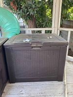 Front view of the outdoor plastic storage box showing textured rattan weave sides and lid with latch handle.