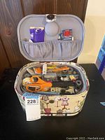 Open sewing kit showing top removable tray with scissors, buttons, bobbins, measuring tape, pins, and other sewing accessories inside fabric-covered case with dress form pattern.