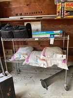 Metal storage rack with three wire shelves and caster wheels. Shows rack from front with some unrelated items on shelves (not included).