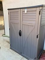 Front view of closed beige resin cabinet with double doors and black handles